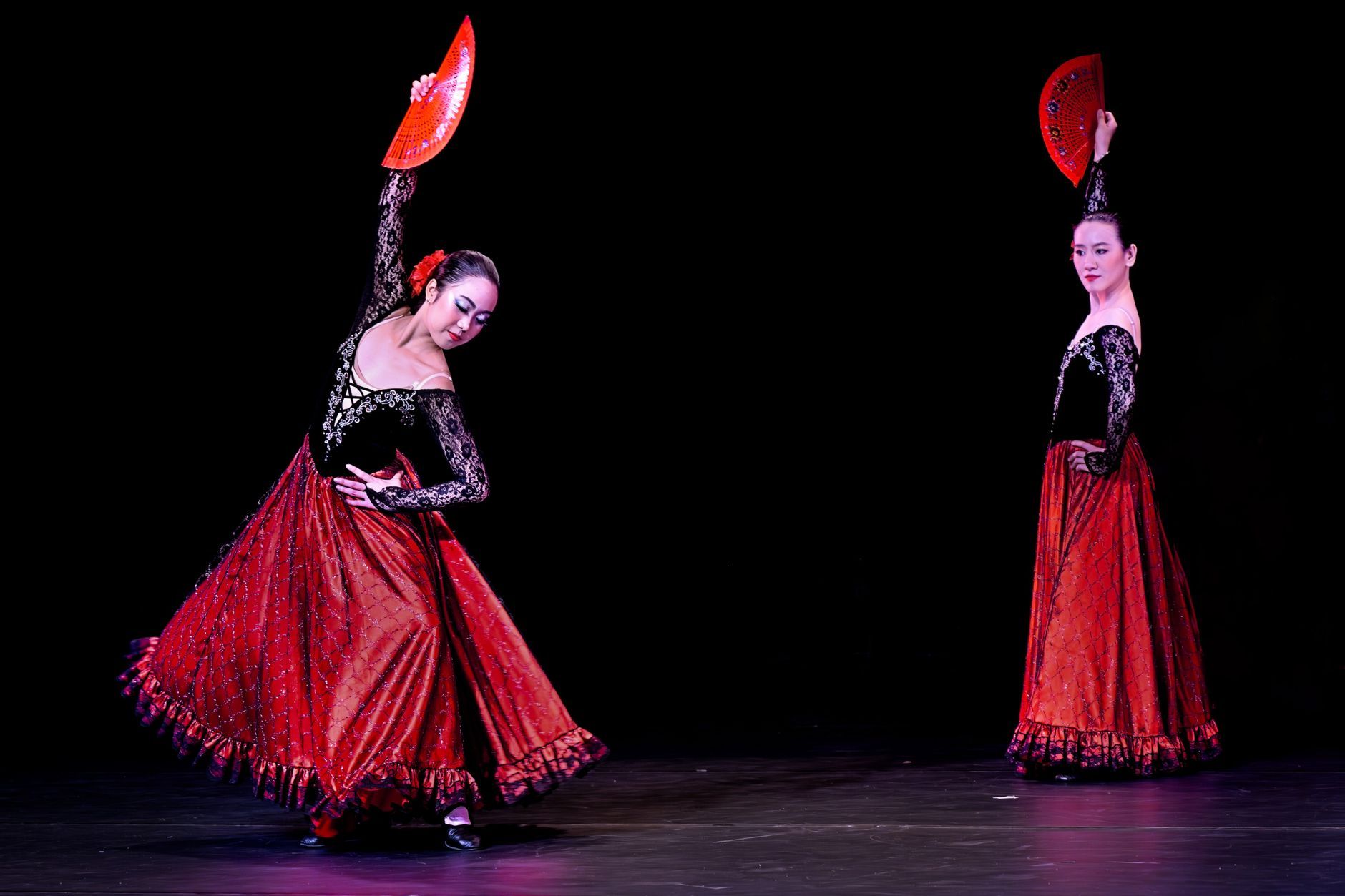 Two flamenco dancers perform with red fans in an elegant show. — peñas y escuelas