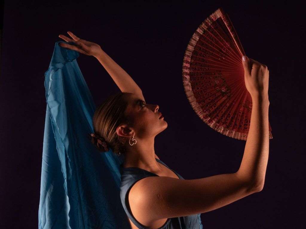 A graceful female flamenco dancer posing with a traditional fan and vibrant fabric.